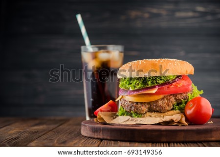 Delicious fresh burger with tomato and cheese and cola glass on background. Fastfood concept dinner