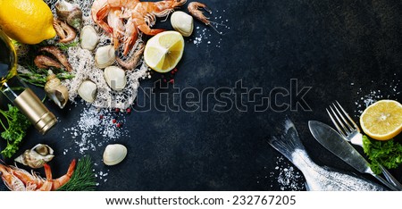 Delicious fresh fish and seafood on dark vintage background. Fish, clams and  shrimps with aromatic herbs, spices and vegetables - healthy food, diet or cooking concept