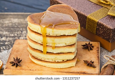 Delicious and fresh pancakes with honey, cooked in the shape of a heart on a dark wooden table. Breakfast for the beloved. 
