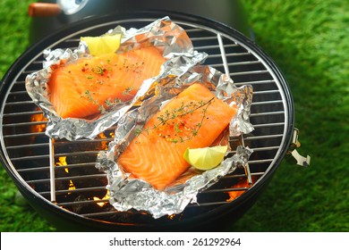 Delicious Fresh Salmon Fillets Grilling On An Open Fire In A Portable Barbecue Lying On Tin Foil Wrappers And Flavored With Fresh Lemon