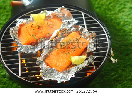 Delicious fresh salmon fillets grilling on an open fire in a portable barbecue lying on tin foil wrappers and flavored with fresh lemon