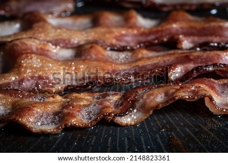 Delicious fried bacon strips over a hot pan