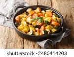 Delicious fried vegetables potatoes, carrots, zucchini and garlic and herbs close-up in a frying pan on a wooden table. Horizontal
