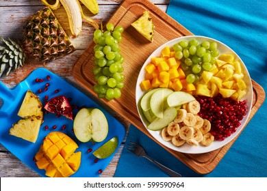 Delicious Fruit Salad With Banana And Green Apple Slices, Chunks Of Mango And Pineapple, Grapes, Seeds Of The Garnet Laid Out On Segments On Platter On Chopping Board, View From Above