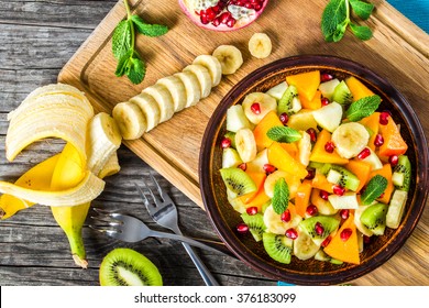 delicious fruit salad in a clay brown dish on a cutting board with two dessert forks, mint leaves, on an old wooden table, close-up, top view - Powered by Shutterstock