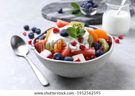 Delicious fruit salad with yogurt on grey table