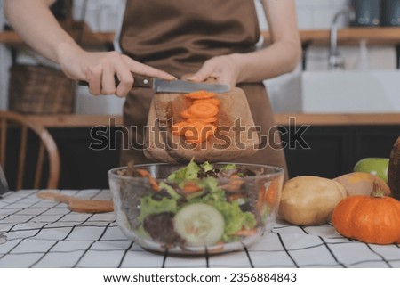 Delicious fruit and vegetables on a table and woman cooking. Housewife is cutting green cucumbers on a wooden board for making fresh salad in the kitchen.