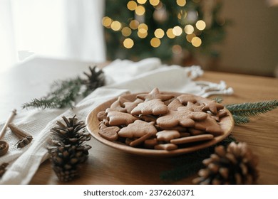 Delicious gingerbread cookies in wooden plate on rustic table against stylish christmas tree lights bokeh. Fresh baked christmas gingerbread cookies, atmospheric holiday time - Powered by Shutterstock