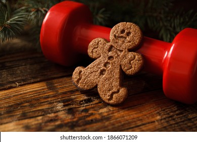 Delicious gingerbread man cookie, heavy red dumbbell and Christmas tree branches. Healthy fitness lifestyle holiday season concept composition, cheat day temptation vs sticking to the diet.