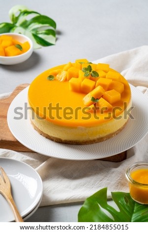 Delicious glazed mango no baked cheese cake with fresh diced mango pulp topping in a plate for serving on bright table background.