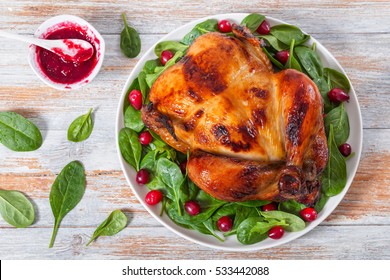 Delicious Golden Crispy Skin Whole Chicken Grilled In Oven And Arugula, Spinach And Cranberry Salad On White Plate On Old White Peeling Paint Boards With Berry Sauce And Green Leaves, View From Above