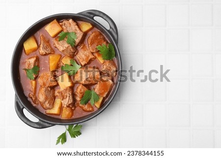 Delicious goulash in pot on white tiled table, top view. Space for text