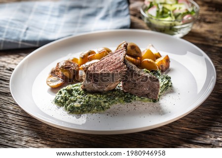Delicious grilled beef sous vide steak served on a white plate with crunchy roasted potatoes, spinach dip and fresh leaf lettuce salad. 