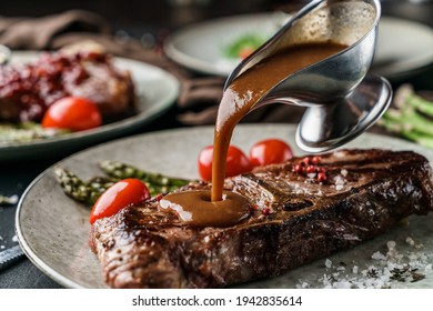 Delicious Grilled Beef Steak With Spices On Plate With Tomatoes And Barbecue Sauce Over Dark Background. Concept Of Bbq Food, Close Up