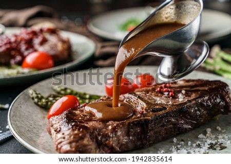 Delicious grilled beef steak with spices on plate with tomatoes and barbecue sauce over dark background. Concept of bbq food, close up