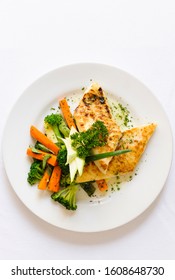 A Delicious Grilled Chicken Fillet Served On A White Plate With Cooked Broccoli And Carrots Aside. On A White Background.