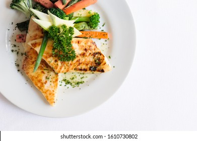 A Delicious Grilled Chicken Fillet Served On A White Plate With Cooked Broccoli And Carrots Aside. On A White Background.