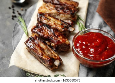 Delicious grilled ribs with sauce served on grey table, closeup
