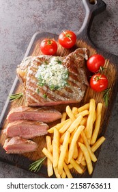 Delicious grilled steak frites with French fries and green butter closeup on the wooden board on the table. Vertical top view from above