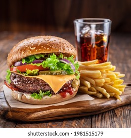 Delicious hamburger with cola and potato fries on a wooden table with a dark brown background behind. Fast food concept. - Powered by Shutterstock