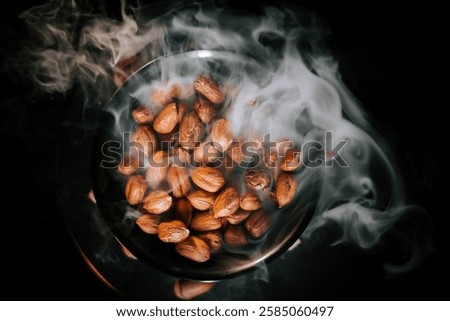 Delicious hazelnuts served in a dark ceramic plate with smoke rising on a black background to enhance presentation