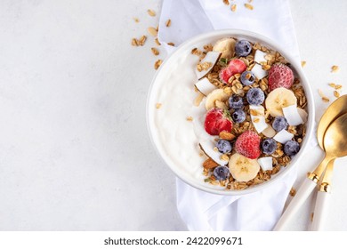 Delicious healthy balanced breakfast or lunch yogurt granola bowl with fruit and berry - banana, strawberry, blueberry, almond, coconut slices copy space - Powered by Shutterstock