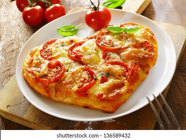 Delicious Heart Shaped Italian Pizza With A Topping Of Tomato And Melted Cheese Served On A Plain White Plate With A Fresh Tomato And Basil