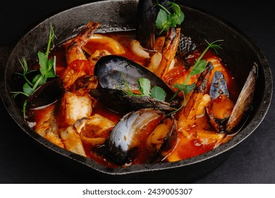 A delicious and hearty seafood stew made with shrimp, mussels, clams, and calamari in a rich tomato broth. The dish is garnished with fresh herbs and served in a cast iron skillet. - Powered by Shutterstock