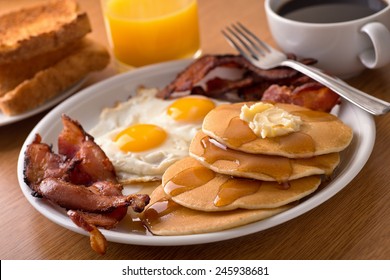 A delicious home style breakfast with crispy bacon, eggs, pancakes, toast, coffee, and orange juice.