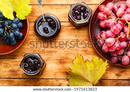 Delicious homemade autumn grape jam on old wooden background.Jar of berry jam