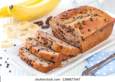 Delicious homemade banana bread with chocolate chips sliced on a white serving tray with ingredients at the background