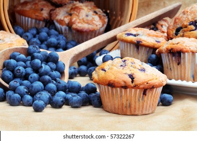Delicious homemade blueberry muffins with fresh blueberries spilling from a wooden spoon and wicker basket.