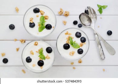 Delicious Homemade Dessert Granola And Blueberry Yogurt Parfait In Glass With Mint On White Wood Boards. Concept Of Light Dessert. Top Down View. Flat Lay. Selective Focus.