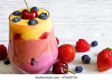 Delicious Homemade Layered Smoothie Dessert Made From Mango, Peaches, Raspberry, Strawberry And Blueberry With Fresh Berries In A Glass. Close Up. Healthy Breakfast. Close Up