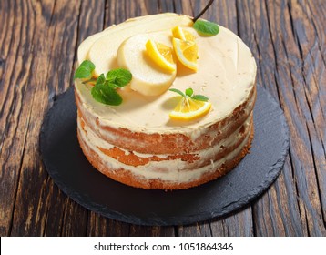 delicious homemade pear sponge cake with whipped cream cheese, decorated with mint leaves, pear and lemon slices on a black slate plate, on wooden table,.view from above
