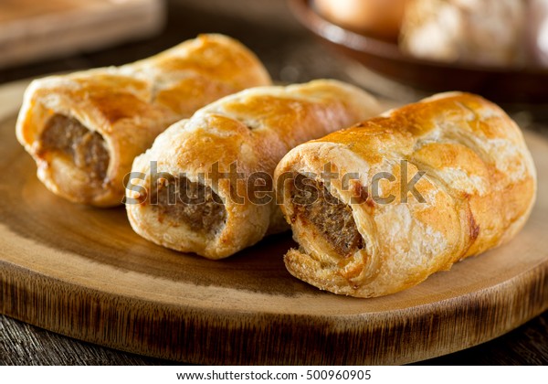 Delicious homemade sausage rolls on a wooden\
serving platter.