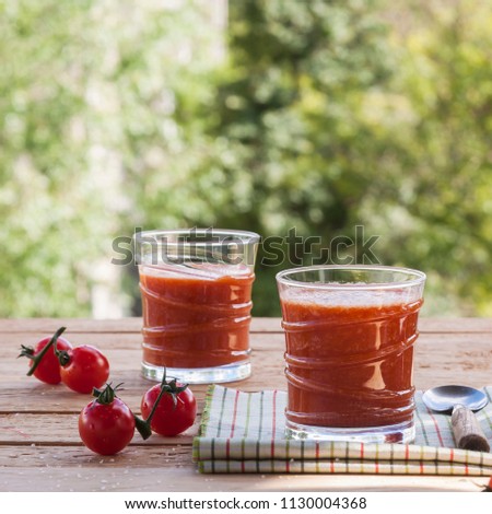 Delicious homemade tomato juice with salt on a striped napkin on a wooden table on a green foliage background. Selective focus. Close up.