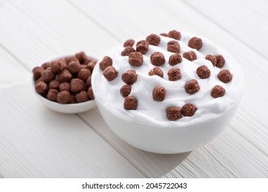 Delicious homemade yogurt with chocolate balls. White wooden background.