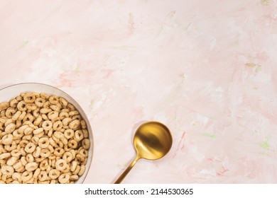 Delicious Honey Cheerios Cereal In A Bowl And Golden Spoon On Pink Background. Top View, Copy Space