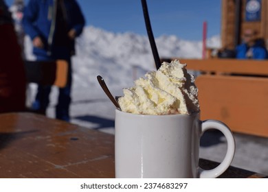 Delicious hot chocolate outdoors in snowy ski resort. Fluffy whipped cream in blank white mug with snowcapped mountain background. Ideal hot drink for a rest during skiing and snowboarding holiday - Powered by Shutterstock