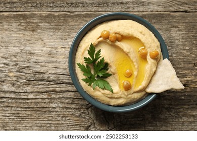 Delicious hummus with olive oil, chickpeas and pita in bowl on wooden table, top view