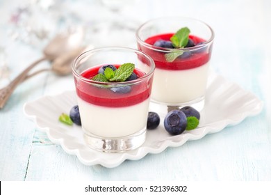 Delicious Italian dessert Panna Cotta with raspberry coulis and fresh blueberries served for two in small transparent glasses