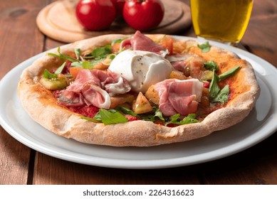 Delicious italian gourmet pizza with sliced raw prosciutto, rocket salad, tomato sauce and buffalo mozzarella 