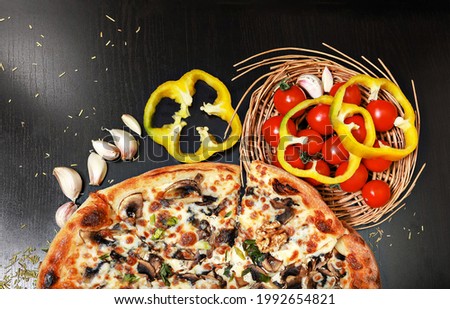 Delicious italian pizza on a black table with vegetables: cherry tomatoes, yellow chopped peppers, garlic and walnuts. Copyspace, top view, flat lay, close-up, horizontal