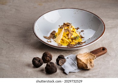 Delicious Italian Tagliatelle or Fettuccine pasta with shaved parmesan cheese and truffle mushroom. Black Truffle and White Truffle with shaver as foreground over rustic fabric cloth. Warm earth tone.