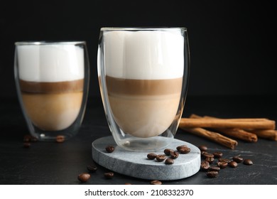 Delicious latte macchiato, cinnamon sticks and coffee beans on black table