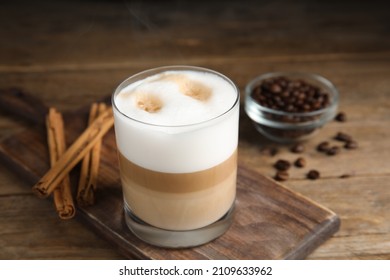 Delicious Latte Macchiato, Cinnamon Sticks And Coffee Beans On Wooden Table