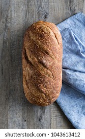 Delicious loaf of artisan sourdough bread on rustic wood bench with blue cloth, top view, copy space