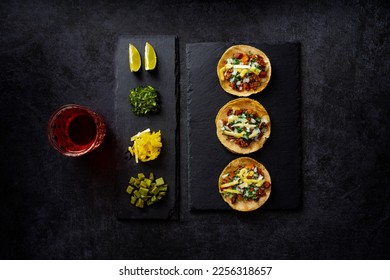 Delicious lunch with tacos and sauces on black table, top view of appetizing Mexican tacos served on black plate near bowl with tomato sauce and avocado placed on wooden table