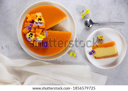 Delicious mango cheesecake cut in slices topping with mango slices and edible flower view from above, close-up, copy space